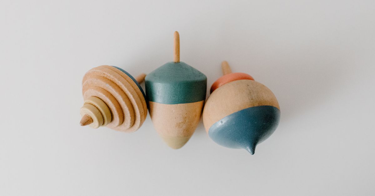 Close-up of three colorful wooden spinning tops on a white surface.